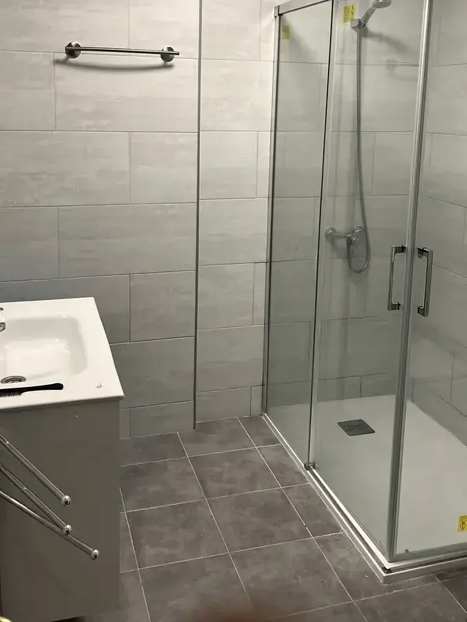 Baño reformado con mampara de ducha, alicatado gris y mueble de lavabo