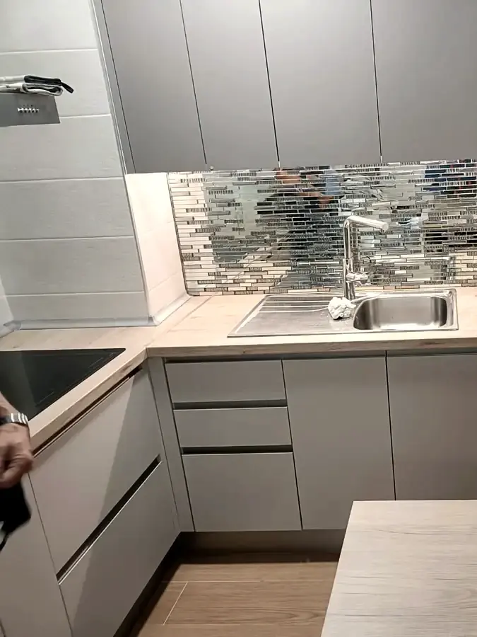 Cocina reformada con muebles grises, encimera de madera y frente de mosaico